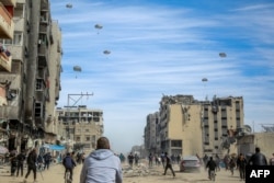Palestinians run along a street as humanitarian aid is airdropped in Gaza City on March 1, 2024