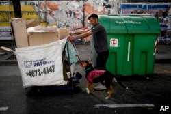 Seorang pria yang mengidentifikasi dirinya hanya sebagai Sebastian berjalan dengan anjingnya Roco saat mencari karton untuk didaur ulang di Buenos Aires, Argentina, 11 Mei 2023. (AP/Natacha Pisarenko)