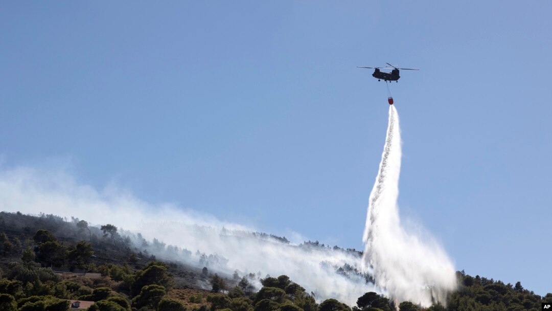 A firefighting helicopter throws water over a wildfire at Keratea area, southeast of Athens, Greece, June 30, 2024. 