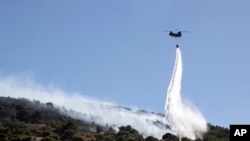 A firefighting helicopter throws water over a wildfire at Keratea area, southeast of Athens, Greece, June 30, 2024. 