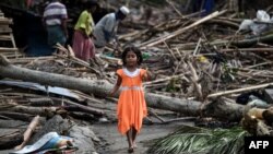 A girl walks past destroyed houses at Basara refugee camp in Sittwe on May 16, 2023, after cyclone Mocha made a landfall.
