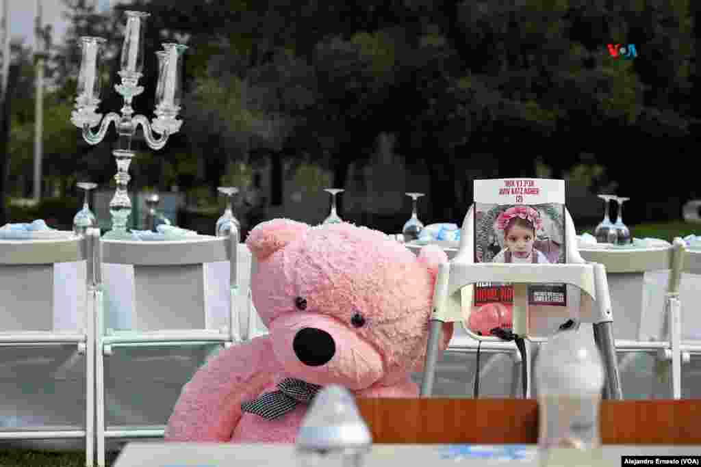 Un oso de peluche permanece junto a la foto de una bebé que permanece secuestrada en Gaza por militantes de Hamás desde hace 20 días. Al fondo, la mesa puesta para todos los secuestrados que aún permanecen en manos de Hamás.