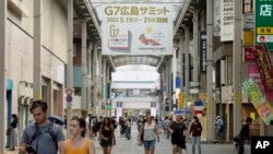 People walk under a banner in a shopping street, announcing the upcoming Group of Seven nations' meetings in Hiroshima, western Japan, May 17, 2023.