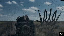 2023 年 8 月 13 日，乌克兰顿涅茨克地区巴赫穆特附近，乌克兰士兵乘坐着一辆装甲运兵车。跟在他们后面的车辆的挡风玻璃上贴着乌克兰国家的象征三叉戟图案。