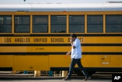 FILE - A Los Angeles Unified School District bus driver walks past parked vehicles at a bus garage in Gardena, Calif., on Dec. 15, 2015. (AP Photo/Damian Dovarganes, File)