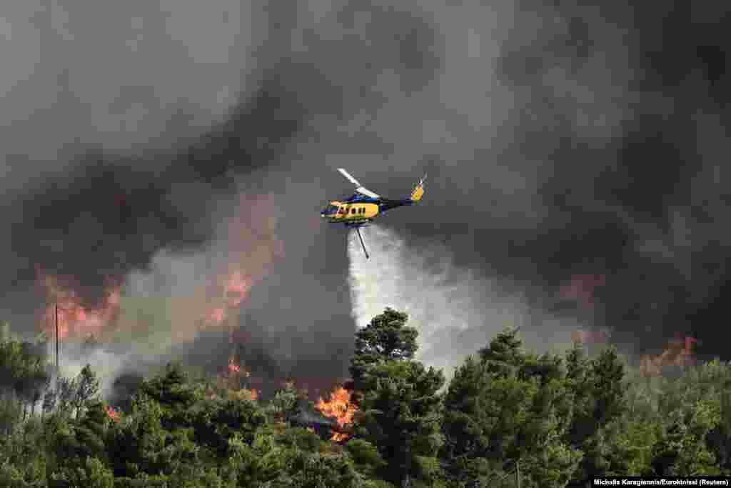 A firefighting helicopter makes a water drop as a wildfire burns in Varnava, near Athens, Greece.