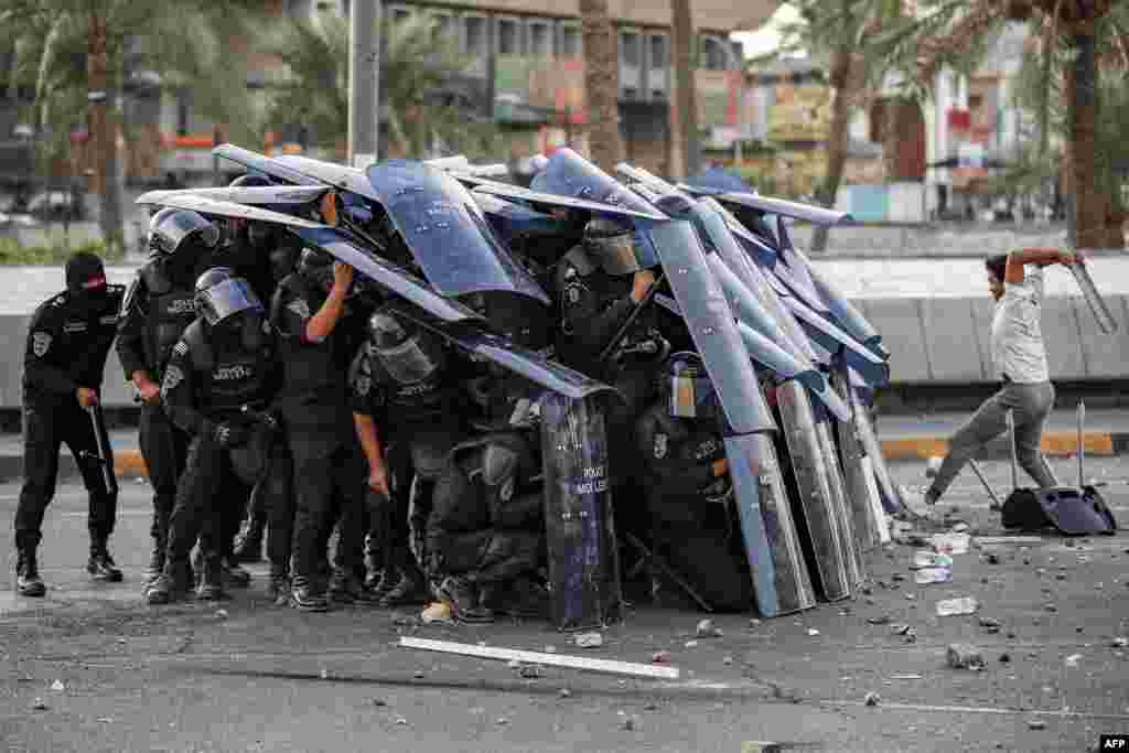 Iraqi riot-control police take cover behind their shields during clashes with protesters gathering on the 4th anniversary of the 2019 Iraqi anti-government demonstrations in Baghdad's Tahrir square, Oct. 1, 2023. 