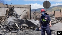 A member of a search-and-rescue team walks along a street, Aug. 12, 2023, in Lahaina, Maui, Hawaii, following heavy damage caused by wildfires.