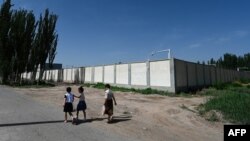 FILE - Children pass an old detention center near Kashgar, China, July 15, 2023. Since 2017, more than a million Uyghurs and other Muslims have been swept into internment camps. Beijing says inhabitants "graduated' and left after learning job skills.