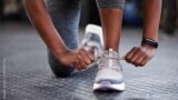 A woman ties up her shoestrings on her sneakers. (Adobe stock image)