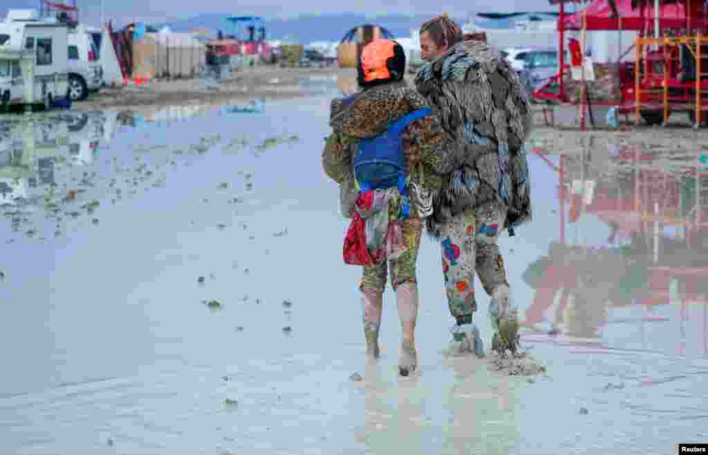 A couple walks through the mud at Burning Man after a night of dancing with friends in Black Rock City, in the Nevada desert, after a rainstorm turned the site into mud, Sept. 2, 2023. (USA Today Network)