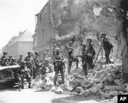 FILE - US soldiers stand on the remains of a house as they inspect damage in Carentan, in the Normandy region of France, June 15, 1944.