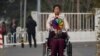 A woman pushes an elderly woman holding a rainbow fan on a street in Beijing, March 5, 2023. China's State Council has issued official "Guidelines for Facilitating the Building of the Basic Elderly Care System" and announced a "List of Basic National Elderly Care Services."