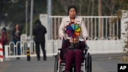 A woman pushes an elderly woman holding a rainbow fan on a street in Beijing, March 5, 2023. China's State Council has issued official "Guidelines for Facilitating the Building of the Basic Elderly Care System" and announced a "List of Basic National Elderly Care Services."