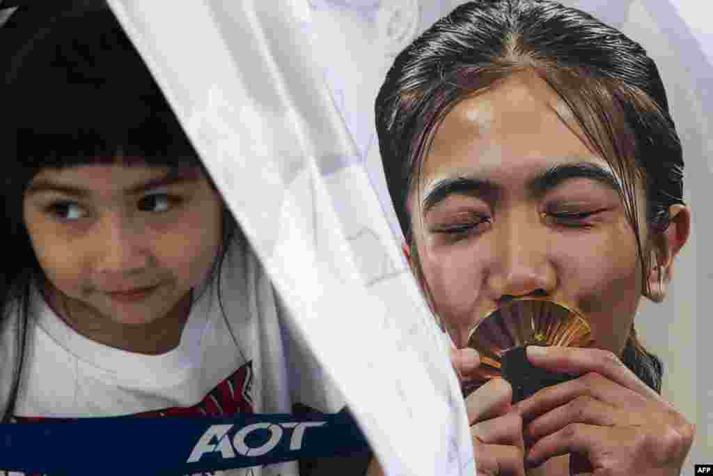 A child, left, stands behind a banner of Thailand's taekwondo gold medalist Panipak Wongpattanakit while waiting to greet athletes on their return to Thailand from the Paris 2024 Olympic Games, at Suvarnabhumi International Airport in Bangkok.