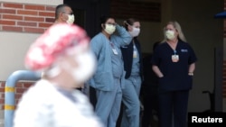 FILE - Nurses stand in a hospital doorway watching a nurses’ protest demanding better personal protective equipment, at UCLA Medical Center, during the coronavirus pandemic, in Los Angeles, California, April 13, 2020.