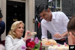 El primer ministro Rishi Sunak sostiene un plato de sándwiches mientras la primera dama de EEUU, Jill Biden, toma uno con una bandera británica mientras asisten a la fiesta Big Lunch en Downing Street en Londres el domingo 7 de mayo de 2023.