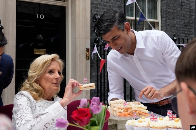 El primer ministro Rishi Sunak sostiene un plato de sándwiches mientras la primera dama de EEUU, Jill Biden, toma uno con una bandera británica mientras asisten a la fiesta Big Lunch en Downing Street en Londres el domingo 7 de mayo de 2023.