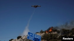 A plane drops water as firefighters try to extinguish a wildfire near the town of Koropi, Greece, June 19, 2024.