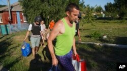 FILE - Villagers carry their belongings as they evacuate from their home village of Monachynivka close to the site of heavy battles against the Russian troops in the Kharkiv region, July 16, 2024. 