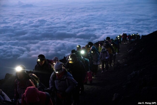 FILE -A group of hikers climb to the top of Mount Fuji just before sunrise as clouds hang below the summit Tuesday, Aug. 27, 2019, in Japan. (AP Photo/Jae C. Hong, File)