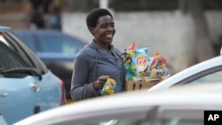 A street trader smiles while greeting motorists on the streets of Harare on May 10, 2023.