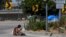 A homeless woman sits on the street at the entrance to an off-ramp to the CA-105 freeway next to a homeless encampment, July 26, 2024, in Los Angeles, California. 