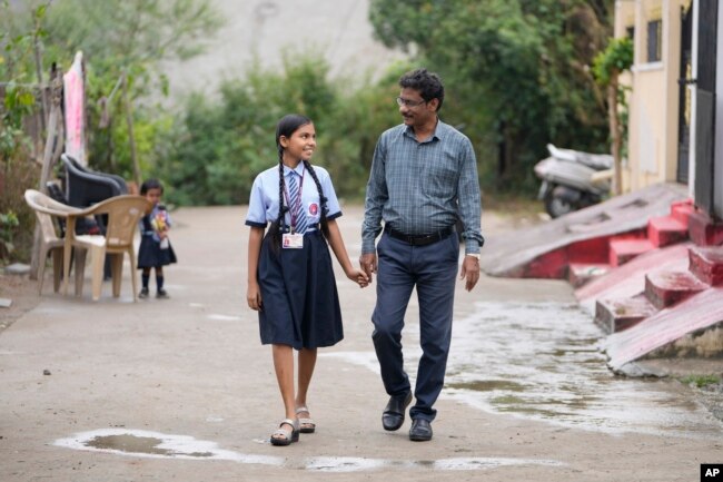 Gautam Dongre, right, of the National Alliance of Sickle Cell Organizations, and his daughter Sumedha, a patient of sickle cell disease walk through their neighborhood in Nagpur, India, Wednesday, Dec. 6, 2023. (AP Photo/Ajit Solanki)