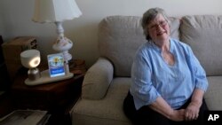 Joyce Loazia poses for a photo next to ElliQ, left, a tabletop device that uses artificial intelligence to conduct human-like conversations, during an interview in her apartment in Coral Springs, Florida, Dec. 5, 2023.