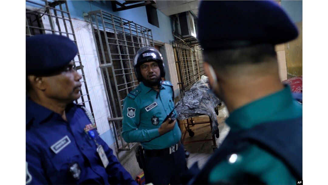 Petugas keamanan berdiri di dekat mayat orang yang tewas dalam kebakaran kereta api di Dhaka, Bangladesh, Selasa, 19 Desember 2023. (AP/Mahmud Hossain Opu)