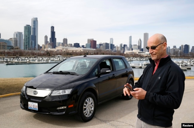 Pengemudi Uber Glen Snower sedang melihat ponselnya di samping mobil listrik BYD e6 di Chicago, Illinois, 18 Maret 2015. (Jim Young/REUTERS)