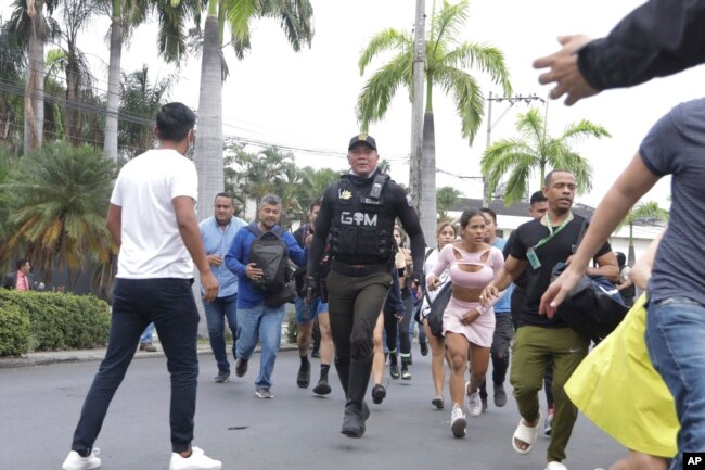 Police evacuate staff from the TC public television station after a group of armed men broke onto their set during a live broadcast, in Guayaquil, Ecuador, Tuesday, Jan. 9, 2024. (AP Photo/Cesar Munoz)