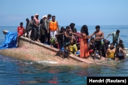 Pengungsi Rohingya berdiri di atas perahu yang terbalik sebelum diselamatkan di perairan Aceh Barat, 21 Maret 2024. (Foto: REUTERS/Hendri)