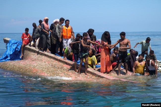 Pengungsi Rohingya berdiri di atas perahu yang terbalik sebelum diselamatkan di perairan Aceh Barat, 21 Maret 2024. (Foto: REUTERS/Hendri)