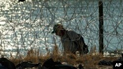 A migrant who crossed the Rio Grande from Mexico to the US seeks a way to pass through concertina wire, Sept. 22, 2023, in Eagle Pass, Texas. 