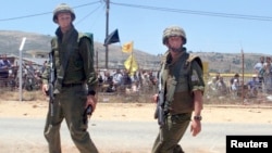 FILE - Israeli soldiers patrol the Israel-Lebanon border while Lebanese wave flags and shout patriotic slogans to celebrate the withdrawal of Israeli troops from south Lebanon, May 26.