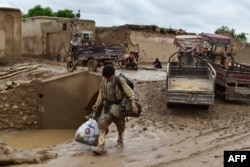 Seorang pria Afghanistan membawa barang-barangnya saat dia berjalan melalui jalan yang tertutup lumpur menyusul banjir bandang setelah hujan lebat di desa Laqiha di distrik Baghlan-i-Markazi di Provinsi Baghlan pada 11 Mei 2024. (Foto: AFP)