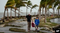 Bob Givehchi, izquierda, y su hijo Daniel, de 8 años, residentes de Toronto que visitan Miami por primera vez, caminan entre escombros y palmeras arrastradas por ráfagas de viento, en Matheson Hammock Park en Coral Gables, Florida, el viernes 15 de diciembre de 2023. 