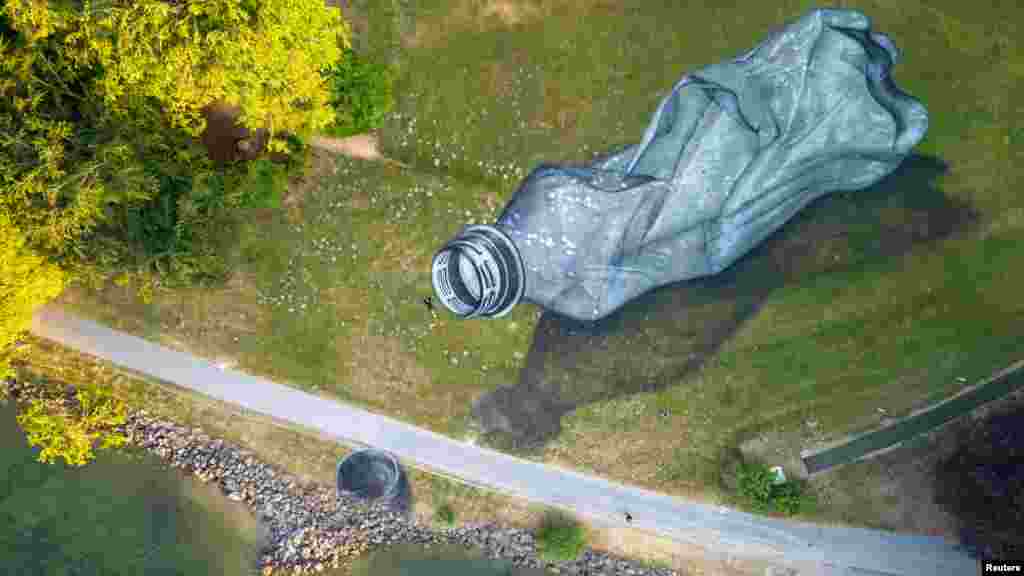 Seniman Swiss-Prancis Saype berpose di samping lukisan seni tanahnya di atas rumput yang menggambarkan botol plastik bekas raksasa, di Parc Bourget di kota Lausanne, Swiss. (Reuters)&nbsp;