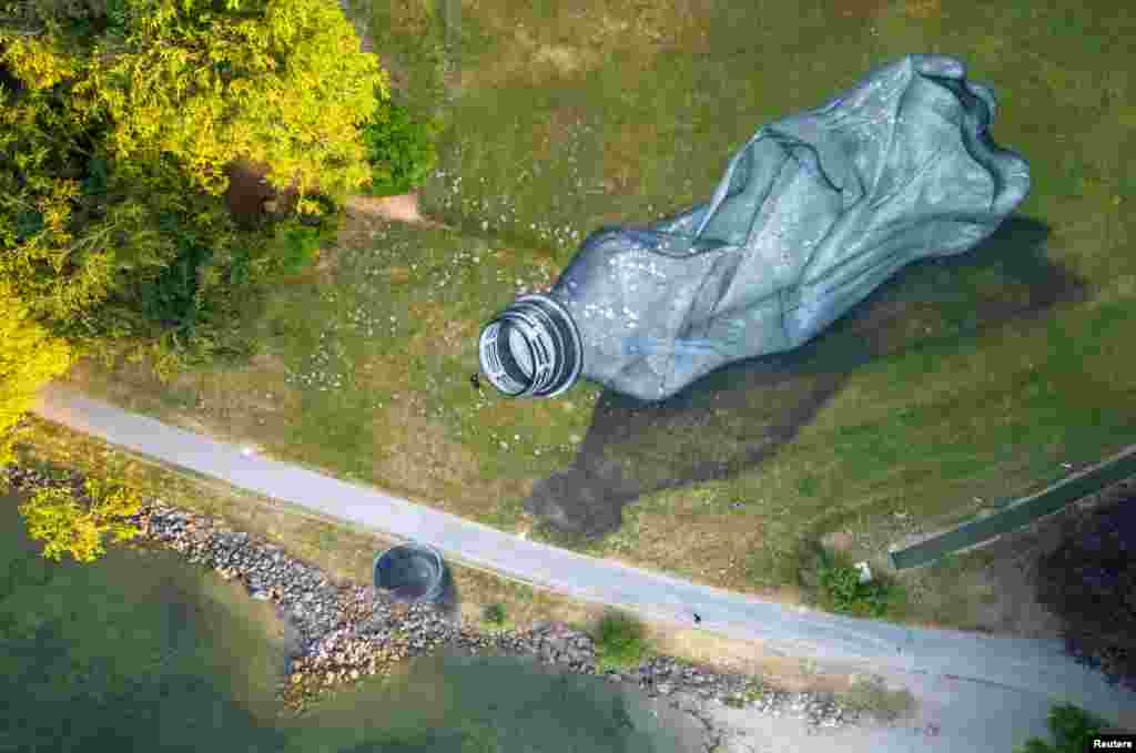 Swiss-French artist Saype poses next to his land art painting on grass representing a discarded plastic bottle, in the Parc Bourget in Lausanne, Switzerland.