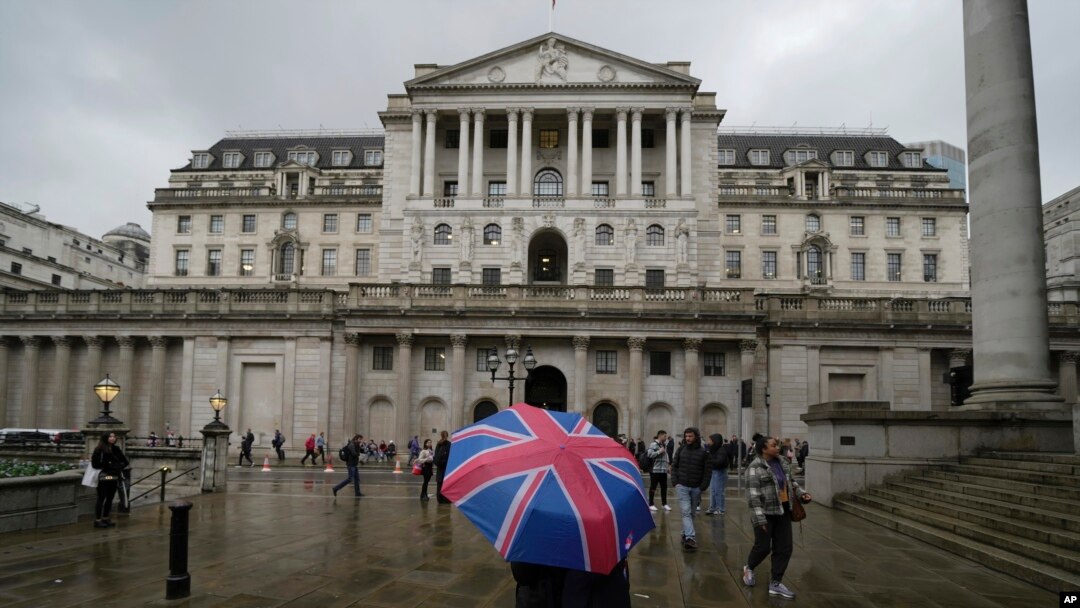 Seorang pengunjung dengan payung bermotif bendera Inggris berdiri di depan gedung bank sentral, Bank of England, di London, 3 November 2022. Bank of England akan menerapkan prosedur kepailitan kepada anak perusahaan Silicon Valley Bank di Inggris. (Foto: Kin Cheung/AP Photo)