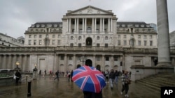 FILE - A woman with an umbrella stands in front of the Bank of England, at the financial district in London, Nov. 3, 2022. The Bank of England said it would put Silicon Valley Bank UK in its insolvency procedure.