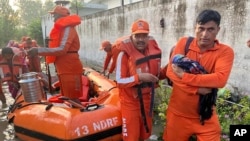 In this photo made available by the National Disaster Response Force (NDRF) on Aug. 15, 2023, an NDRF personnel carries an infant to safety in flood-affected Himachal Pradesh state, India. 