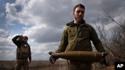 Soldados ucranianos cargan proyectiles para disparar contra posiciones rusas en la línea del frente, cerca de la ciudad de Bájmut, en la región ucraniana de Donetsk, el 25 de marzo de 2024. (Foto AP/Efrem Lukatsky)