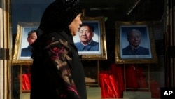 资料照：一名女子走过北京一家商场橱窗里悬挂的中共前领导人毛泽东、刘少奇和周恩来的画像。（2012年11月11日）