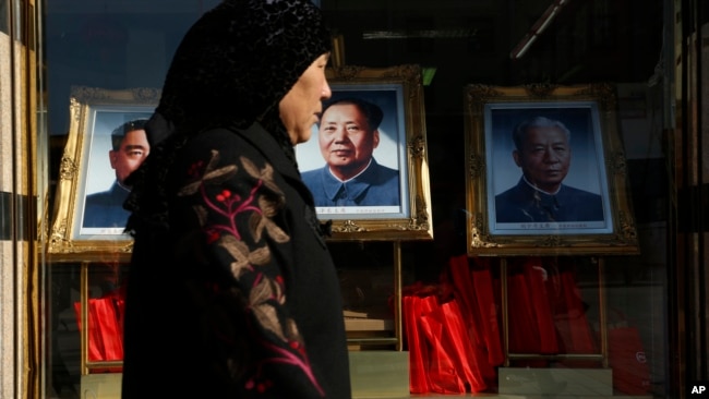 资料照：一名女子走过北京一家商场橱窗里悬挂的中共前领导人毛泽东、刘少奇和周恩来的画像。（2012年11月11日）