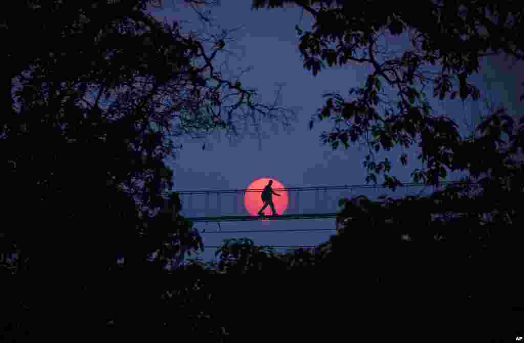 A man crosses a suspension bridge at sunset in Bhaktapur, Nepal.