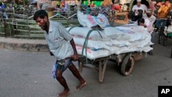 একটি পাইকারি বাজার থেকে চিনির ভারি ব্যাগ বোঝাই একটি ঠেলা গাড়ী টেনে নিয়ে যাচ্ছে বাংলাদেশী একজন শ্রমিক। রবিবার, ১০ এপ্রিল ২০১৬। (ফাইল ছবি) 