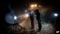 Members of NGOs Deathcare Embalming Team, left, and Turkish Kurt-Ar inspect the bucket of an excavator as they search for bodies of people who died during the earthquake in Kahramanmaras, Turkey, Feb. 17, 2023.