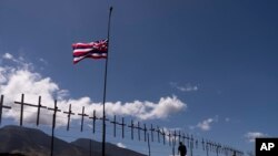 2023年8月22日，夏威夷拉海纳，拉海纳绕道沿线的栅栏上悬挂着纪念近期在野火中遇难者的十字架，夏威夷州的州旗在风中飘扬。(美联社图)